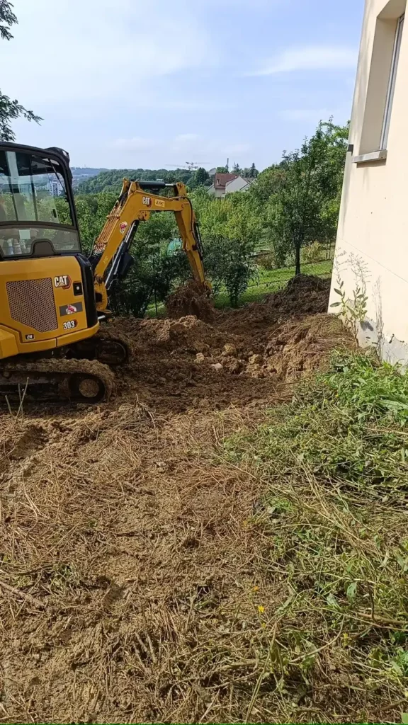 Mini-pelle creusant une tranchée de drainage le long du mur d'une maison, à Pontault-Combault
